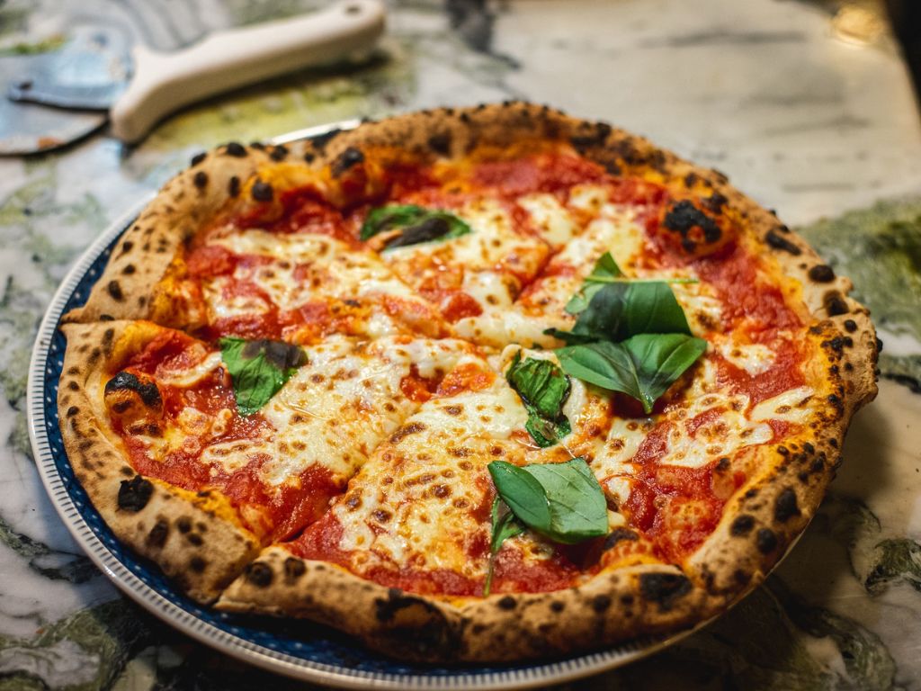 Pizza Margherita is a classic Italian pizza topped with tomato sauce, fresh mozzarella cheese, basil leaves, and a drizzle of olive oil, representing the colors of the Italian flag.
